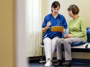 A healthcare professional talks with an older adult patient with a clipboard in hand